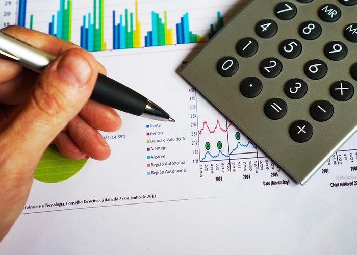 Hand holding a pen next to a calculator valuing a business graph